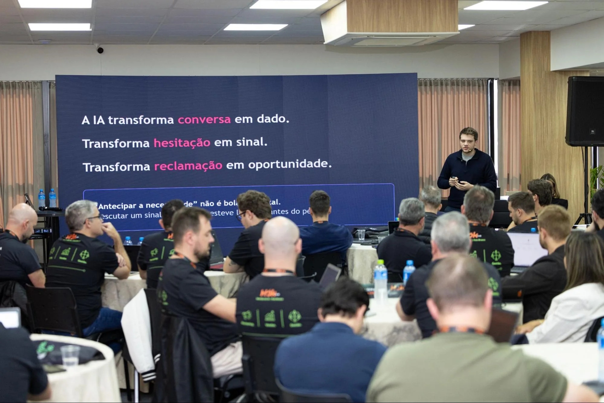 Palestrante ao lado de um telão com frases sobre inteligência artificial, apresentando para uma plateia em um encontro da HOK Master Class
