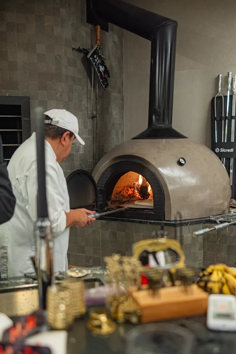 Cozinheiro operando forno de pizza a lenha durante experiência gastronômica do HOK